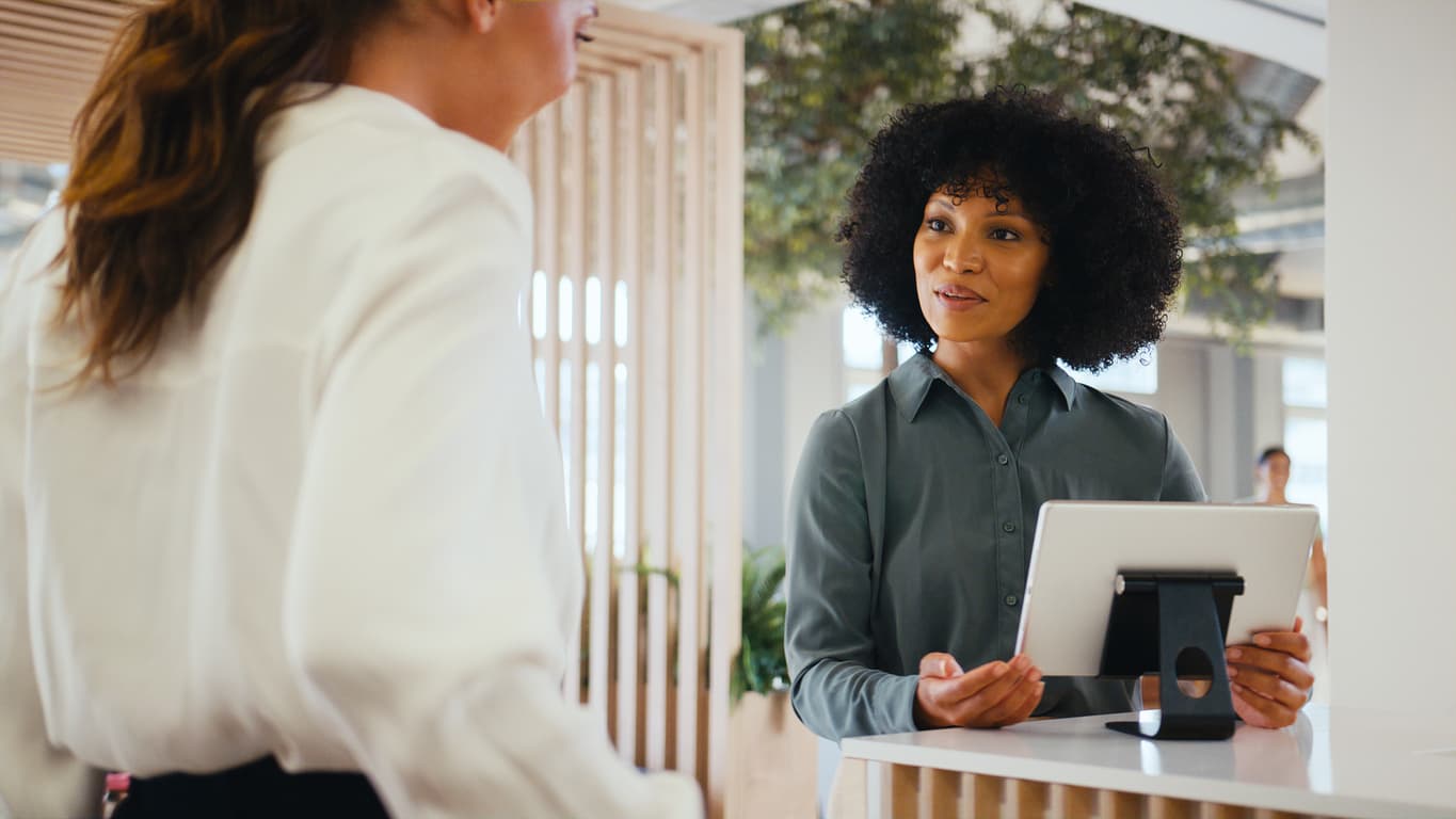 Front-desk staff member reviewing wellness information on a tablet with a client in a bright, modern practice